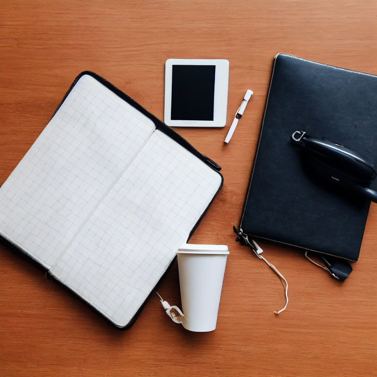 Neatly arranged desk items: notebook, pen, glasses, smartphone, headphones, coffee cup