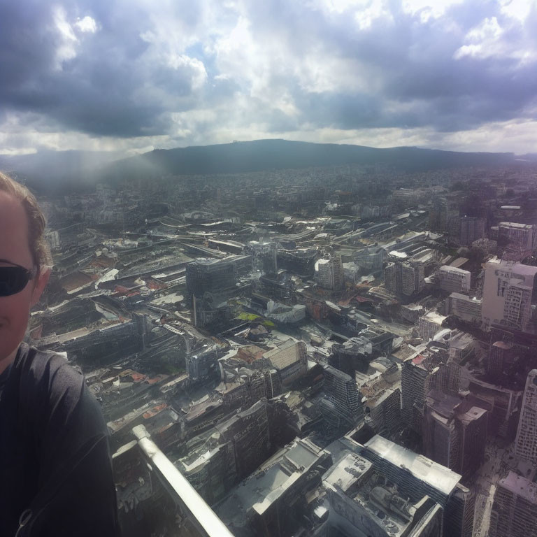 Cloudy cityscape with buildings, person's face, distant mountains, and sunlight.