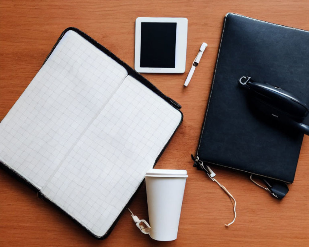 Neatly arranged desk items: notebook, pen, glasses, smartphone, headphones, coffee cup