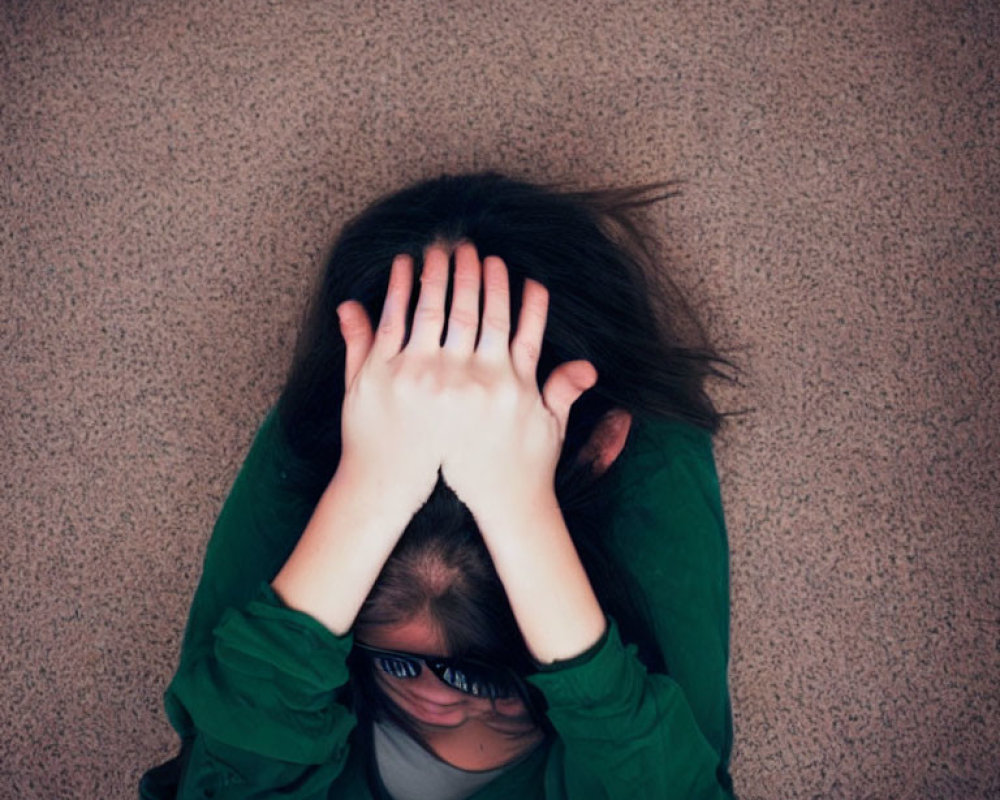 Stressed person in green shirt and glasses sitting on floor