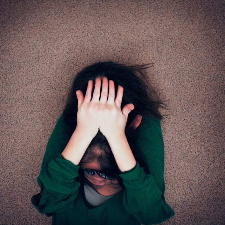 Stressed person in green shirt and glasses sitting on floor