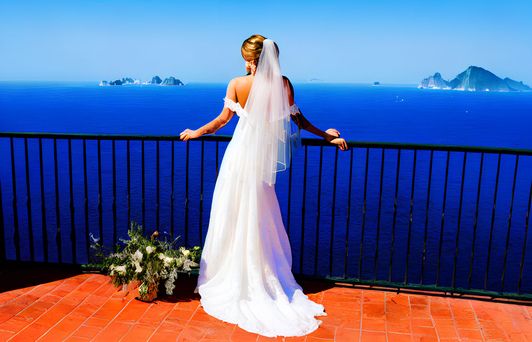 Bride in white wedding dress on terrace overlooking sea with bouquet