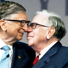 Two older men in glasses, one whispering, in professional attire on blue backdrop