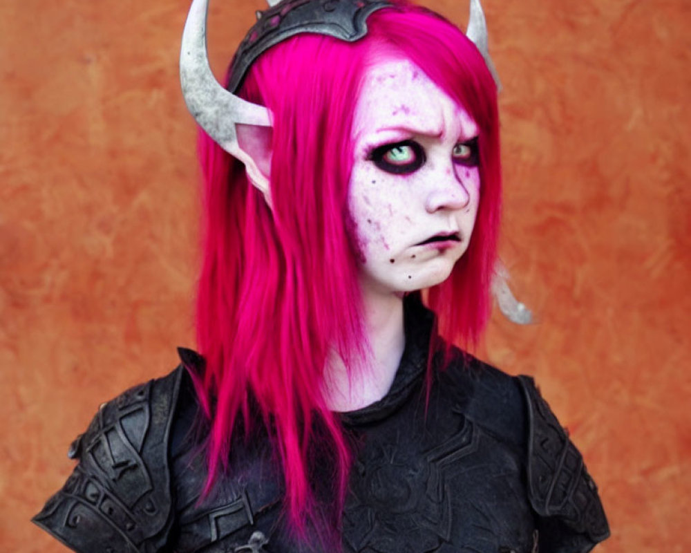 Pink-haired person with demon-like fantasy makeup in dark armor on orange backdrop.