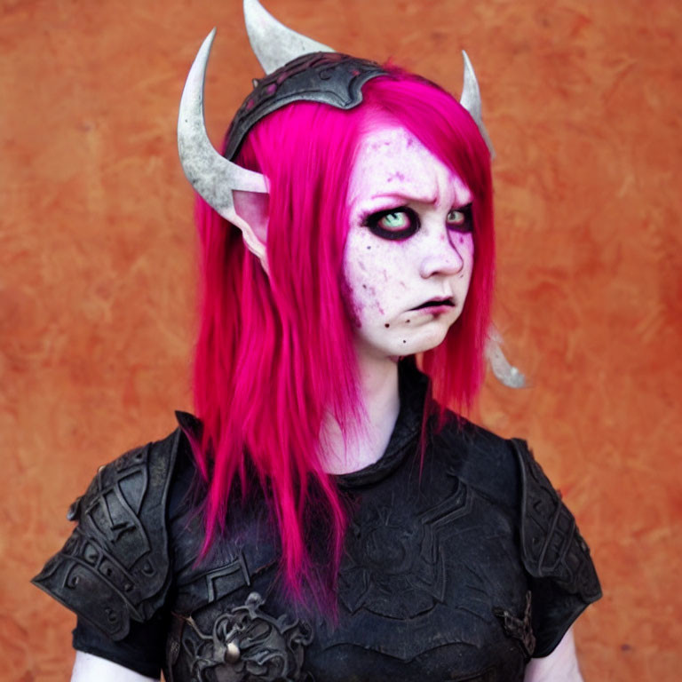 Pink-haired person with demon-like fantasy makeup in dark armor on orange backdrop.