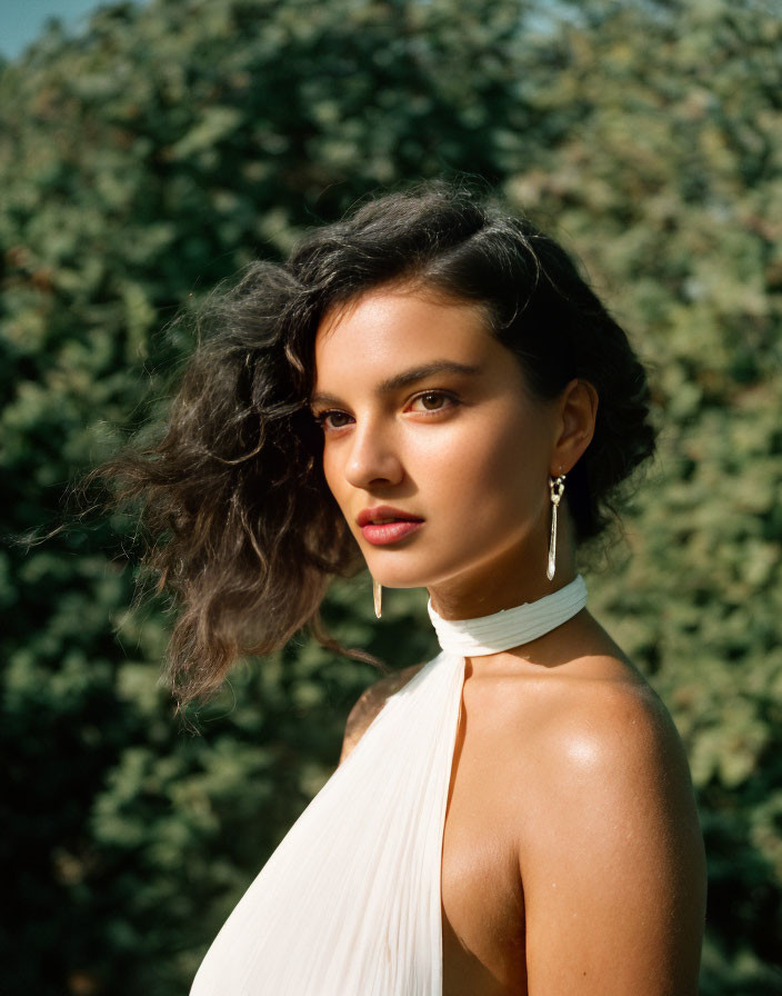 Dark-haired woman in off-shoulder white top against greenery background