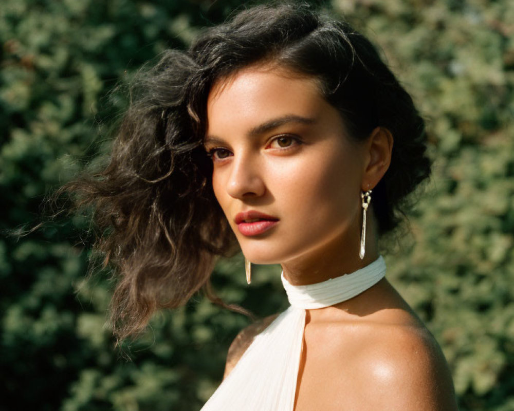 Dark-haired woman in off-shoulder white top against greenery background