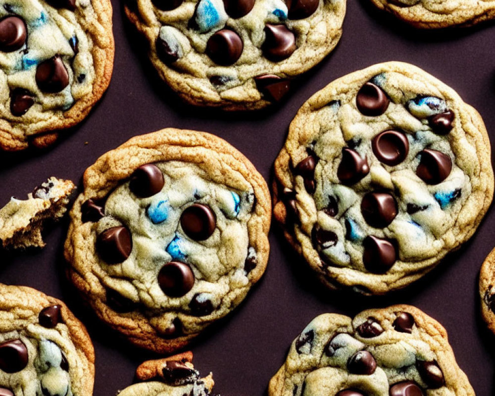 Chocolate chip cookies with regular and blue-colored candies on dark surface