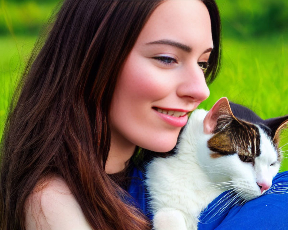 Smiling woman with long brown hair holding a white and brown cat in green field