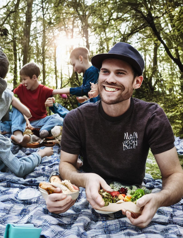 Man in hat smiles at picnic in sunny forest with sandwich and salad.