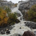 Autumn waterfall landscape with orange trees and misty mountains