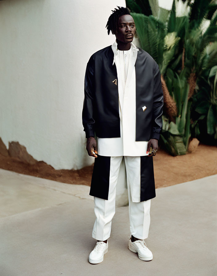 Man in stylish black and white outfit outdoors wearing jacket, shirt, trousers, and sneakers