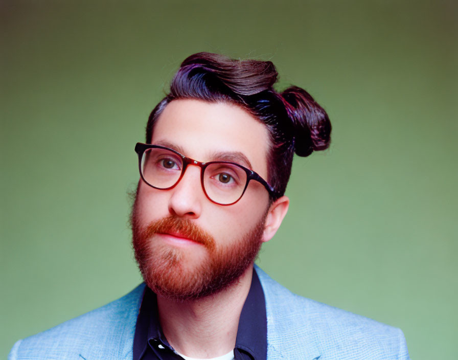 Styled man in blue suit with unique topknot hairstyle on green backdrop