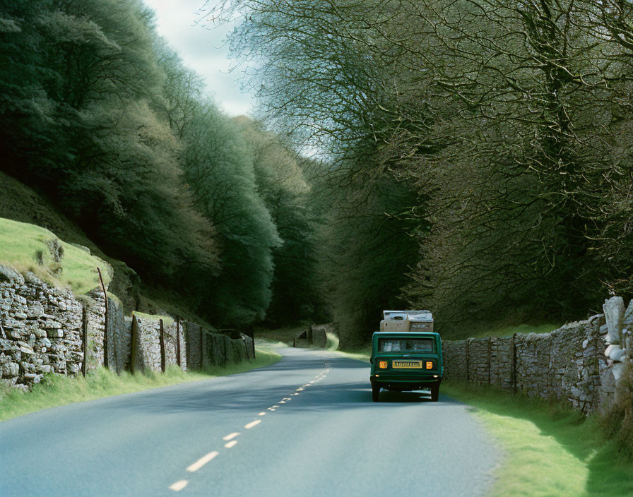 Vintage green van on scenic road with lush trees and stone walls.