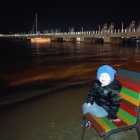 Solitary figure on beach at night under starry sky and bright moon.