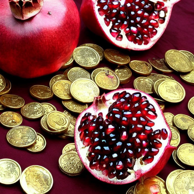 Pomegranates with seeds on maroon surface and golden coins.