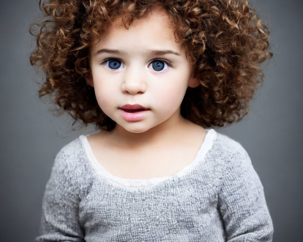 Curly-Haired Child with Blue Eyes in Grey Top