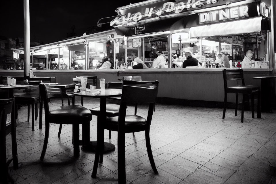 Monochrome night scene of empty diner's outdoor seating area and interior dining.