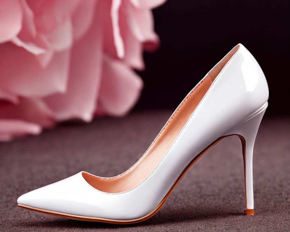 White high-heeled stiletto shoe on soft pink backdrop with floral design