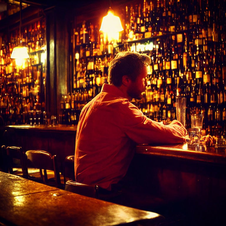 Man in contemplative pose at dimly lit bar with bottles in background