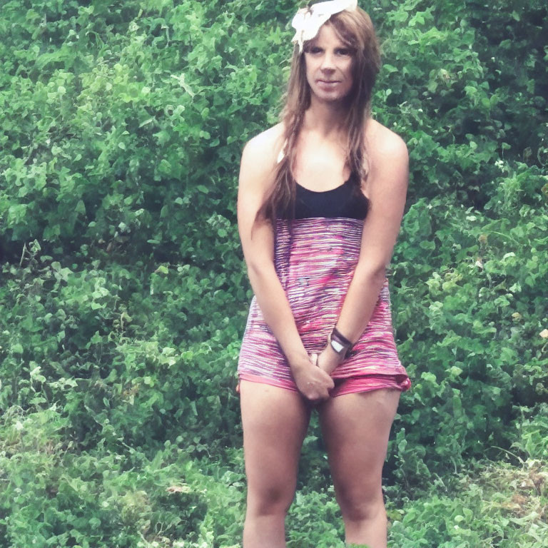 Woman in Sleeveless Striped Dress with White Flower in Hair Against Green Foliage