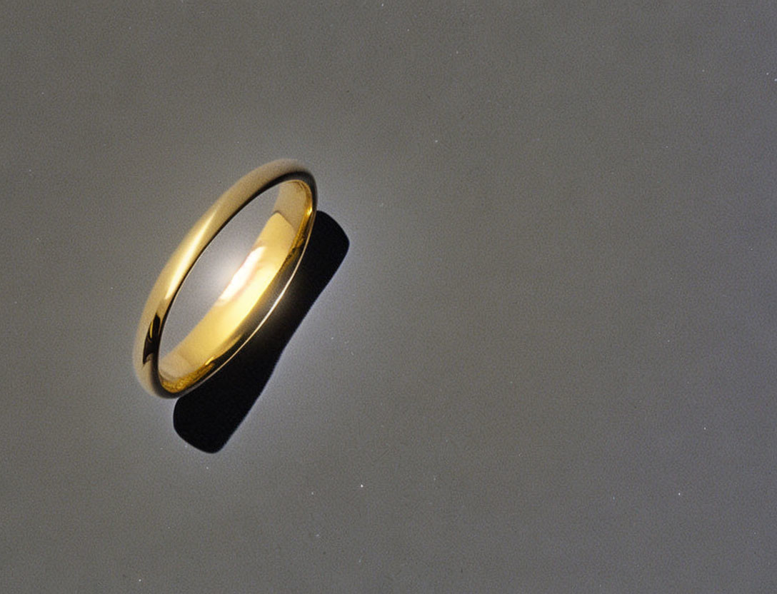 Shiny gold band ring on gradient gray background with light reflection