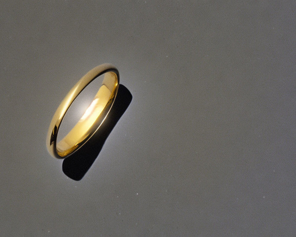 Shiny gold band ring on gradient gray background with light reflection