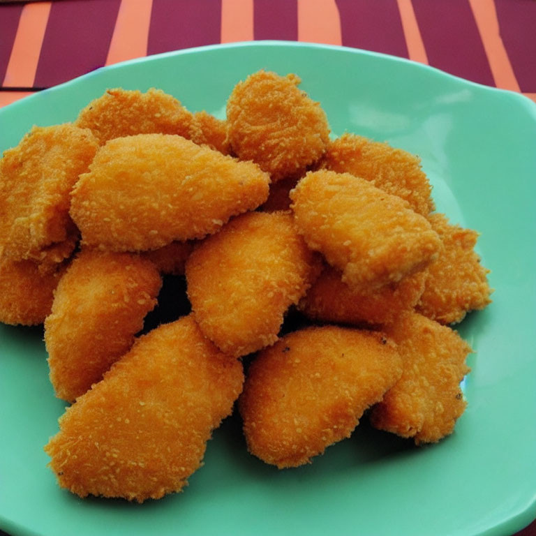 Golden-brown Breaded Chicken Nuggets on Turquoise Plate with Striped Background