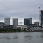 Modern cityscape with unique buildings along a river under cloudy skies