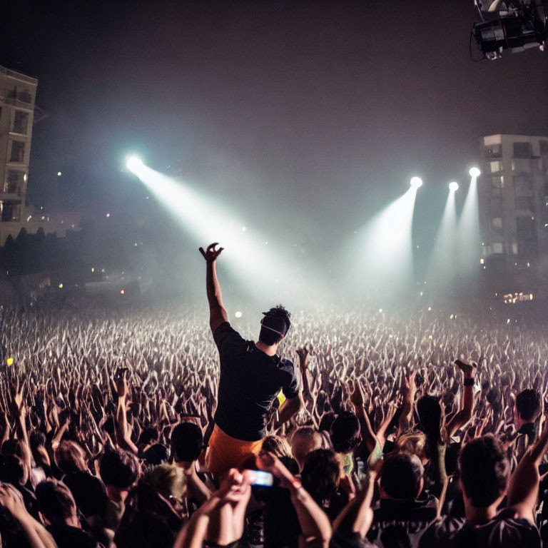 Performer on Stage with Raised Arms and Cheering Crowd at Night