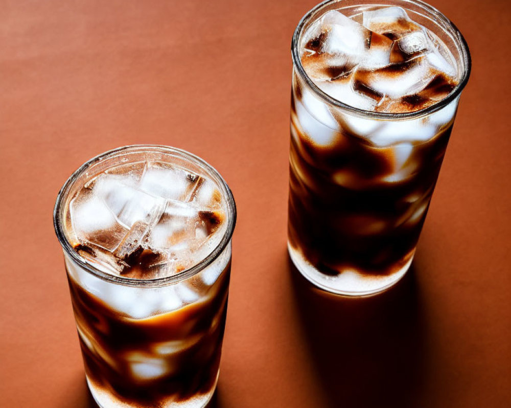 Iced coffee glasses with swirling milk on brown surface