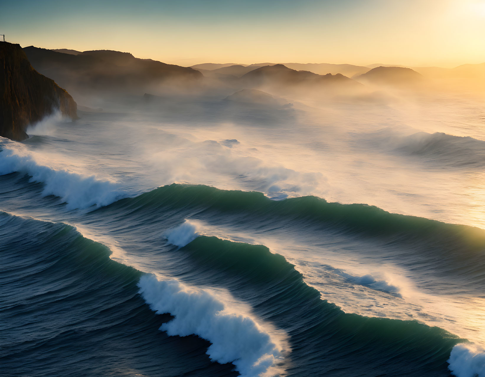 Scenic sunrise over rugged coastline with crashing waves and mist.