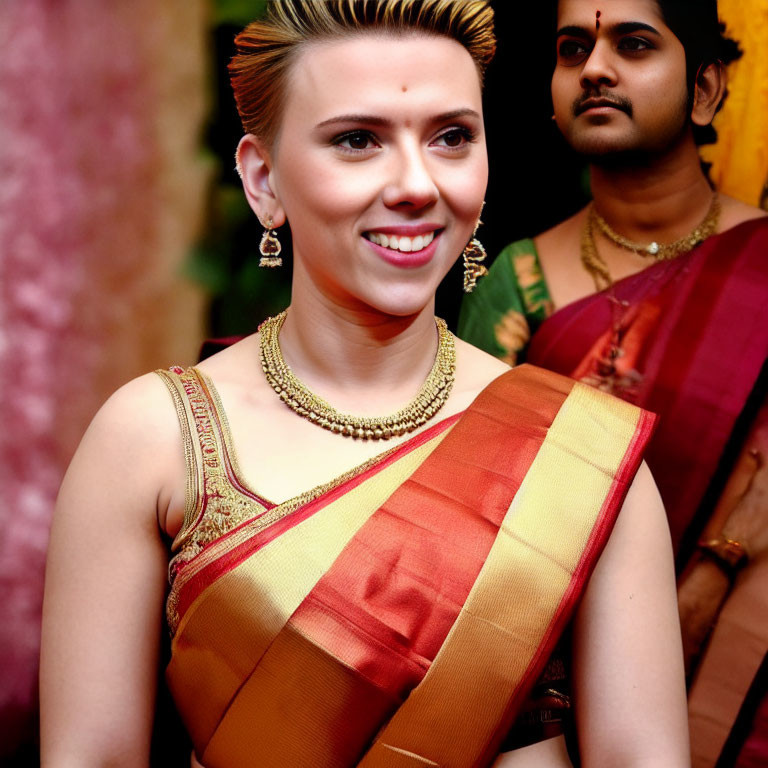 Traditional Indian woman in saree with gold jewelry smiling beside man in background