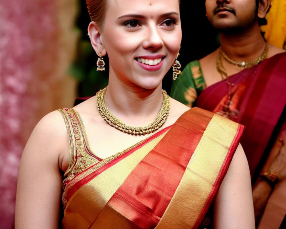 Traditional Indian woman in saree with gold jewelry smiling beside man in background