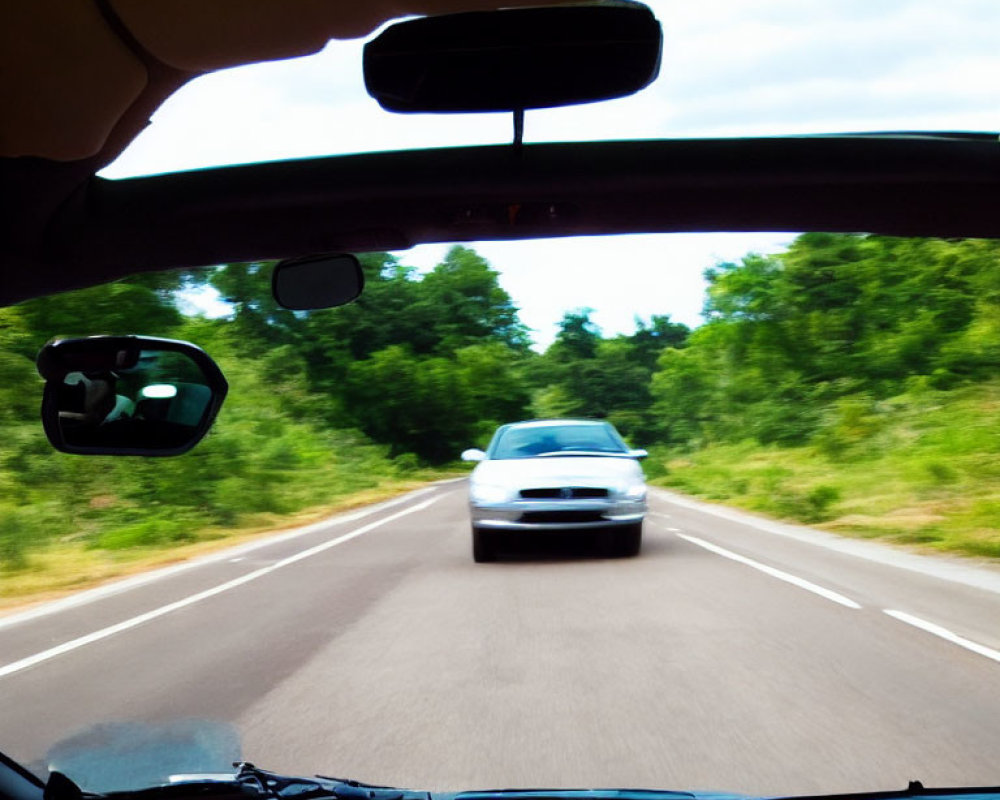 Two-lane road view: Car approaching in daylight with greenery.