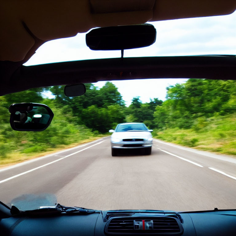 Two-lane road view: Car approaching in daylight with greenery.