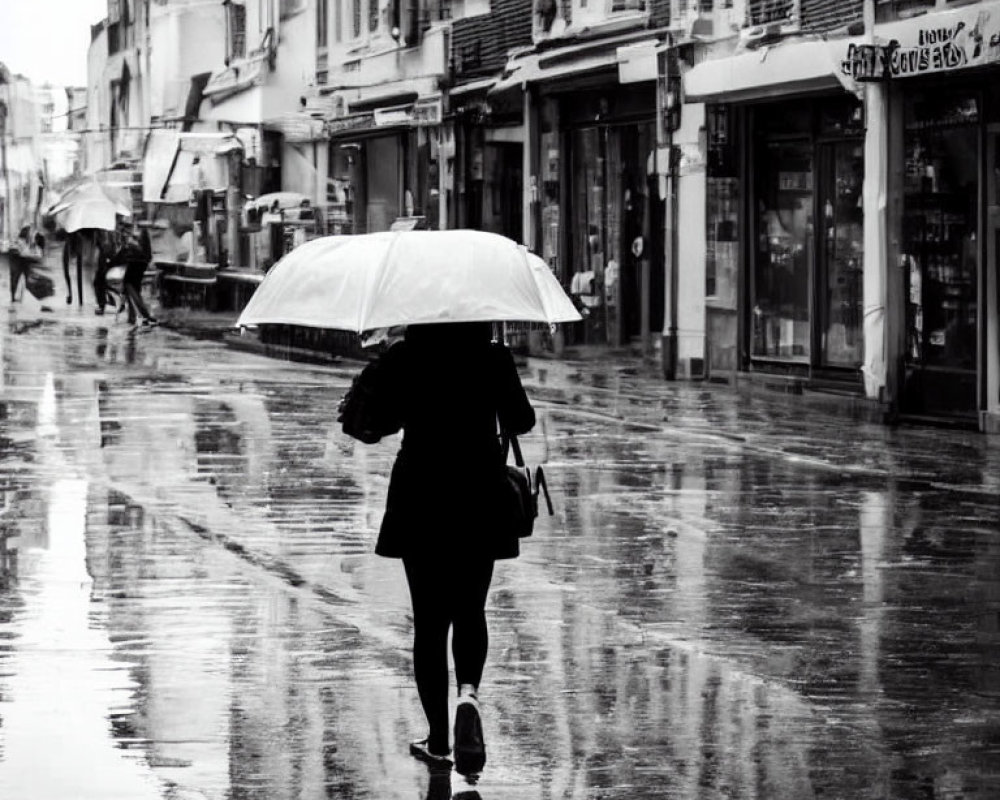 Pedestrian with umbrella walking on wet street under rain, reflecting buildings.