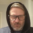 Elderly man with grey hair and beard in glasses and hooded jacket portrait