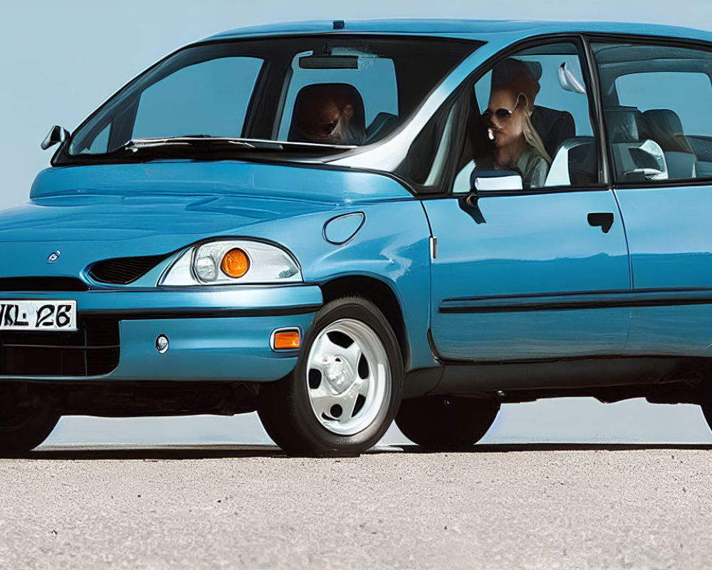 Blue compact hatchback car with two adults wearing sunglasses parked on asphalt under clear sky