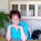 Illustrated elderly woman in blue outfit with medallion at cluttered table