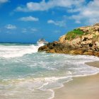 Tranquil beach scene with crashing waves, rocky cliff, green foliage