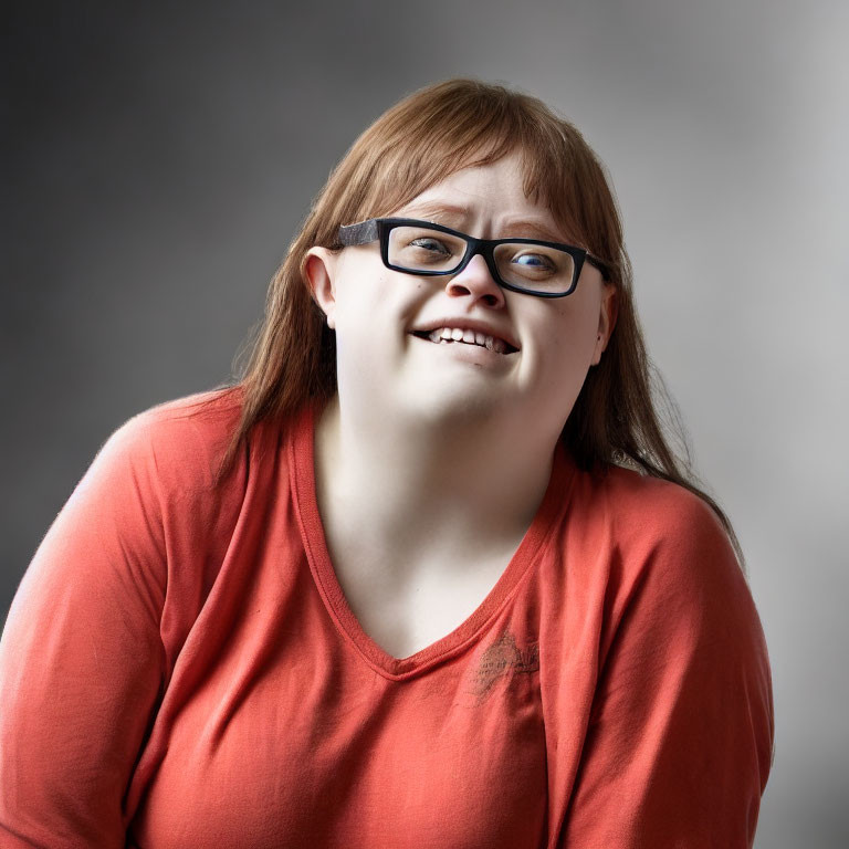 Smiling person with glasses in orange top on grey background