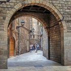 Stone Archway Over Cobblestone Street and Old Buildings with Pedestrians, Lanterns, and