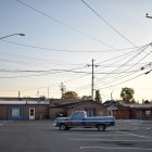 Vintage shops, classic car, and power lines in urban street painting.