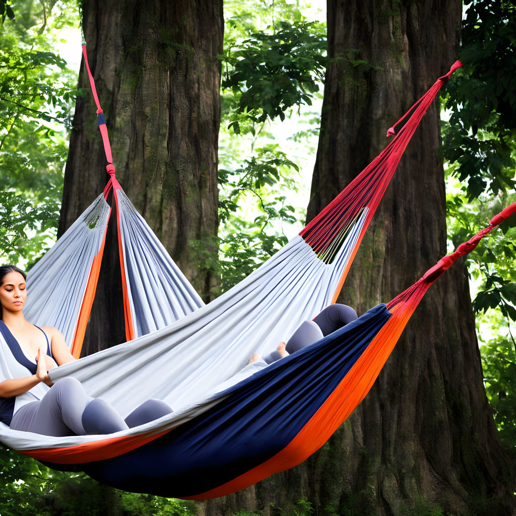 Person meditating in striped hammock among lush green foliage