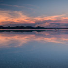 Tranquil landscape with reflective lake, orange clouds, blue sky, and distant mountains.