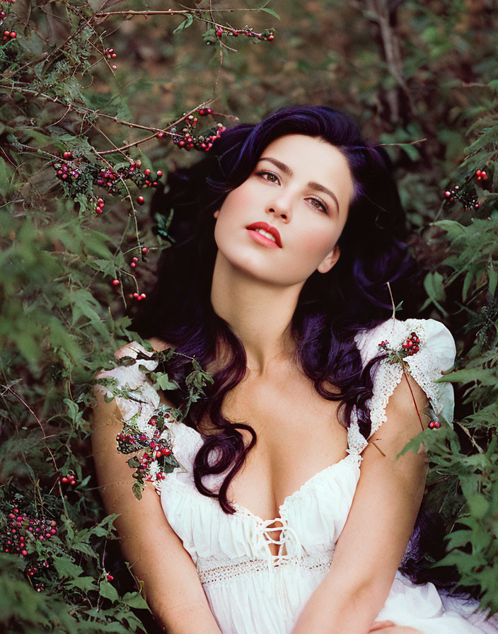 Dark-haired woman in white dress amidst green foliage and red berries.