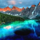 Serene lake reflecting blue flowers and trees amidst mountainous backdrop