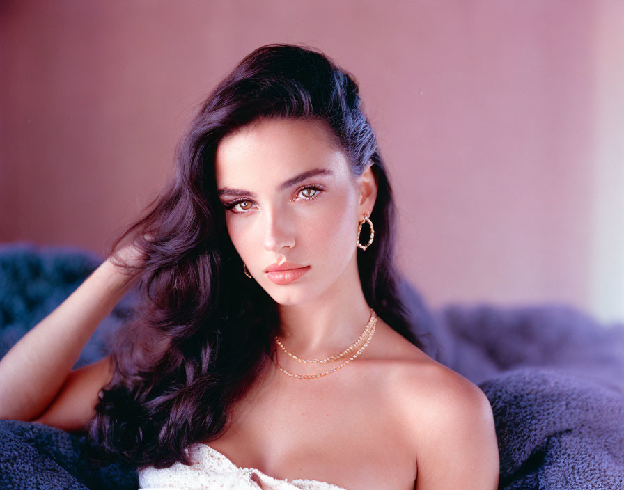 Dark-haired woman in gold earrings posing against pink background