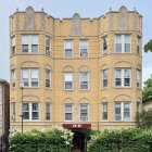 Historic sandstone building with ornate windows, balconies, and lush garden under blue sky